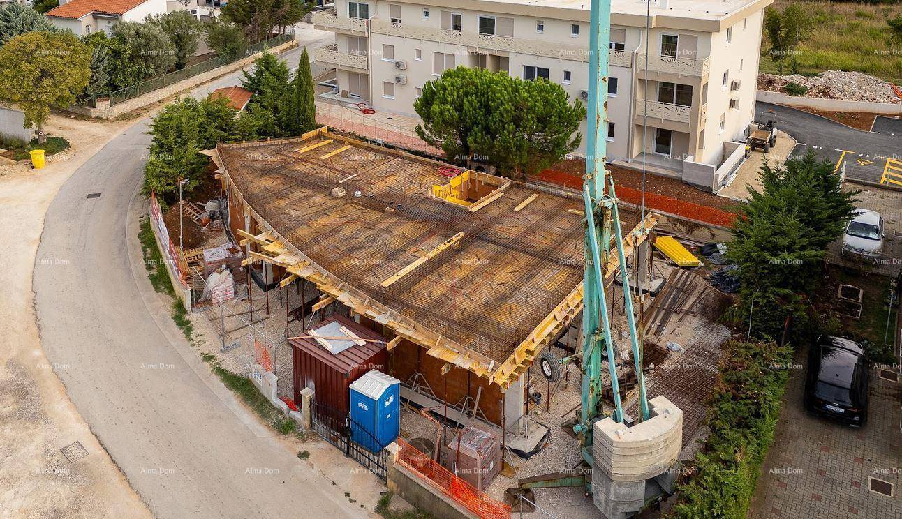 Übersicht der Baustelle mit Rohbau, Betonpumpe und umliegenden Gebäuden unter blauem Himmel.