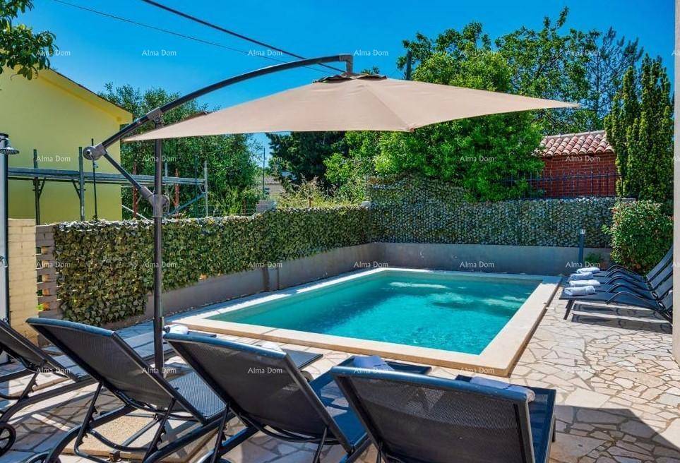 Entspannender Poolbereich mit Liegestühlen und großem Sonnenschirm an einem sonnigen Tag.