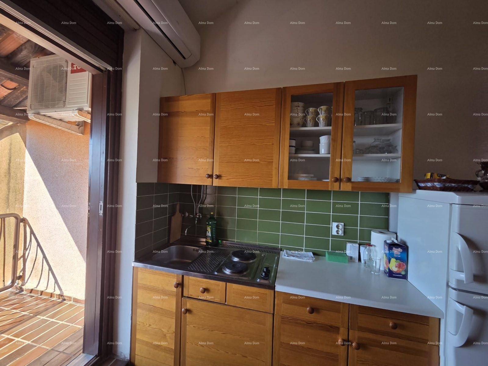 Kleine Küchenzeile mit Holzschränken, grünen Fliesen und Zugang zu einem Balkon.