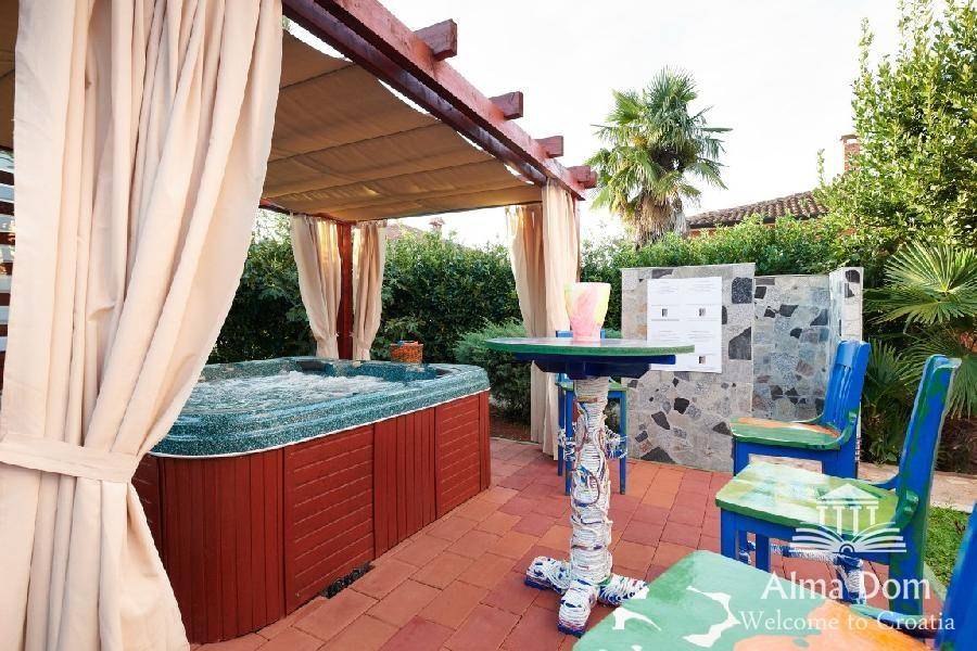Überdachter Whirlpool unter einer Pergola mit Vorhängen und einem kleinen Sitzbereich.