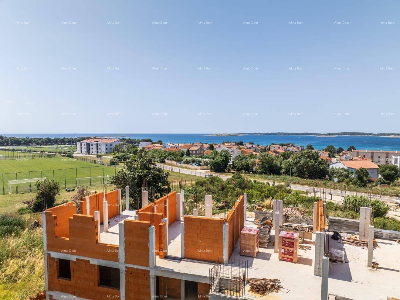 Blick von der Baustelle auf das Meer, den Sportplatz und die umliegende Küstenlandschaft.