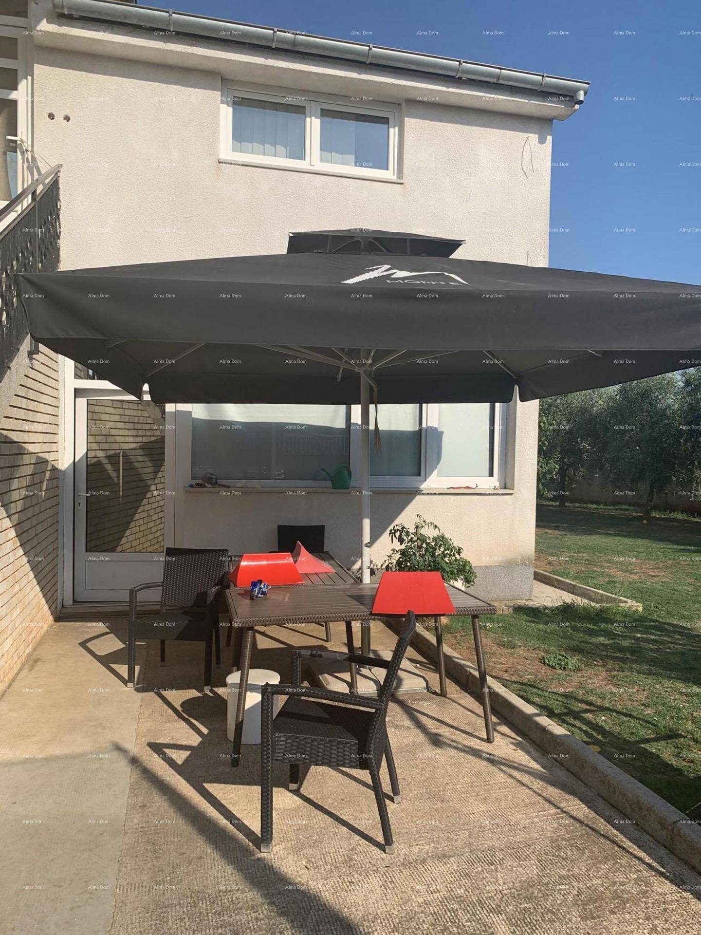 Gemütliche Terrasse mit Esstisch, Stühlen und großem schwarzen Sonnenschirm neben dem Haus.