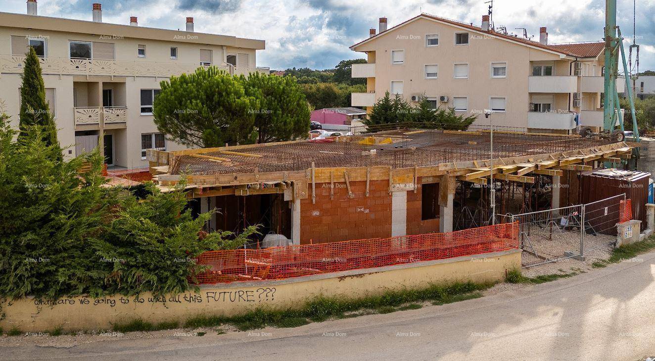 Seitenansicht der Baustelle mit dem Rohbau des Erdgeschosses und umliegenden Wohngebäuden im Hintergrund.