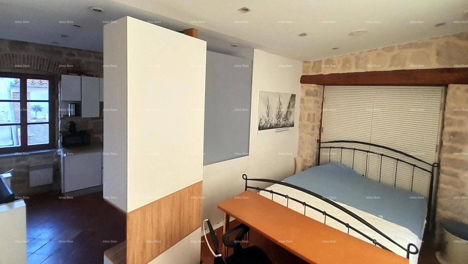 Schlafbereich mit Bett, Schreibtisch und rustikaler Steinwand, offen zur Küchenzeile.