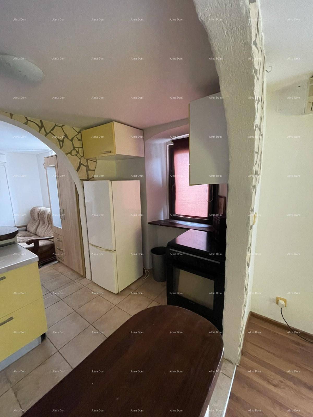 Küchenzeile mit Kühlschrank und Herd, durch einen Steinbogen mit dem angrenzenden Wohnraum verbunden.