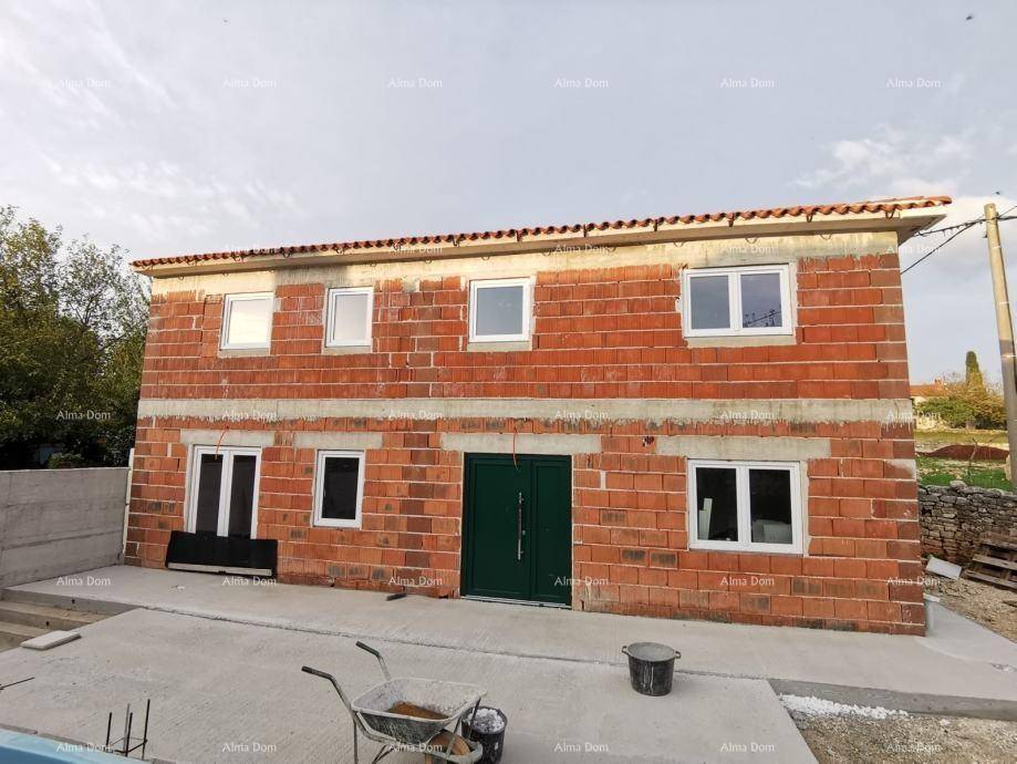 Rohbau eines Hauses mit roten Ziegelwänden, weißen Fenstern und grüner Eingangstür.