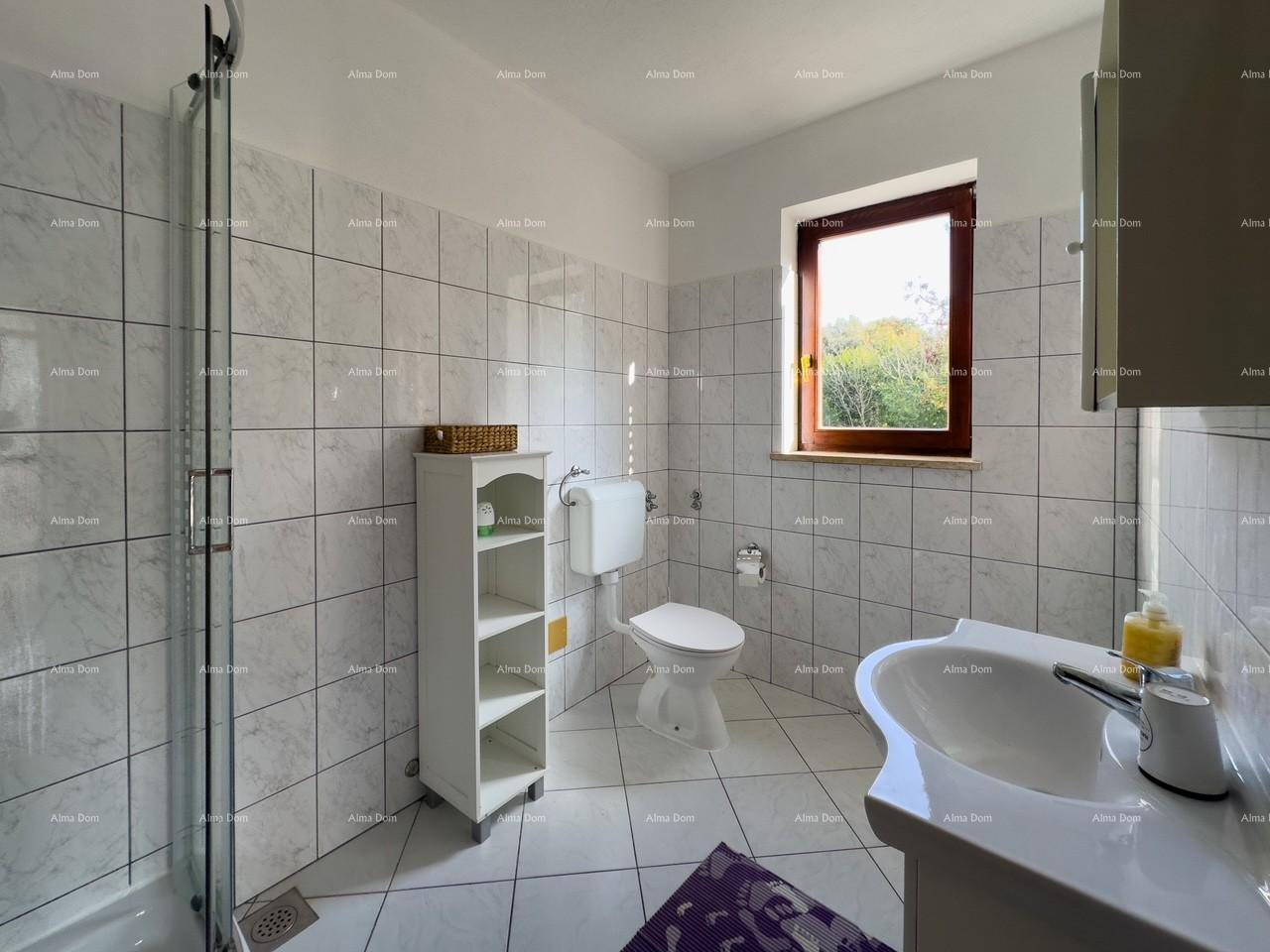 Badezimmer mit weißen Fliesen an Wänden und Boden, Duschkabine, Toilette, Waschbecken und Fenster.