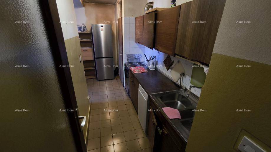 Funktionale Küche mit älteren Holzschränken, Spüle und Kühlschrank.