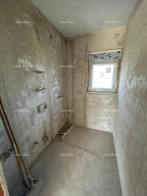 Kleiner, unfertiger Raum mit vorbereiteten Sanitäranschlüssen und einem Fenster, ideal für ein Badezimmer.