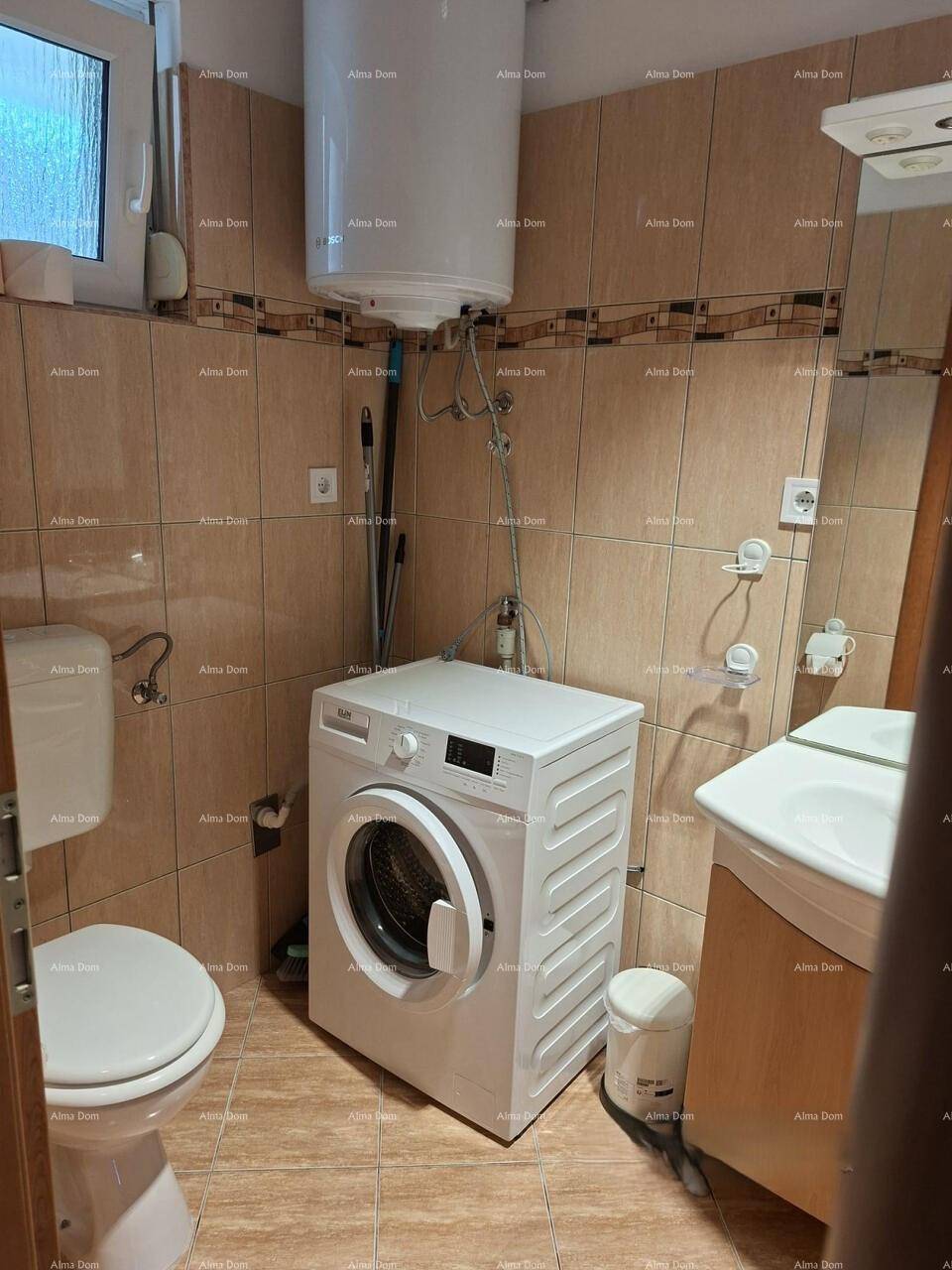 Badezimmer mit WC, Waschbecken, Waschmaschine und Fliesen an Wänden und Boden.