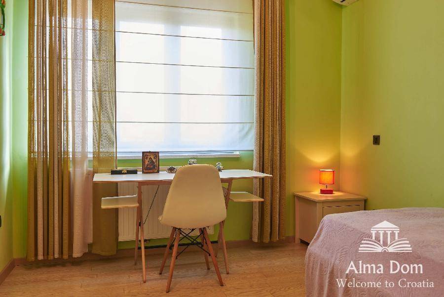 Helles Zimmer mit Schreibtisch, Stuhl und großem Fenster für viel Tageslicht.