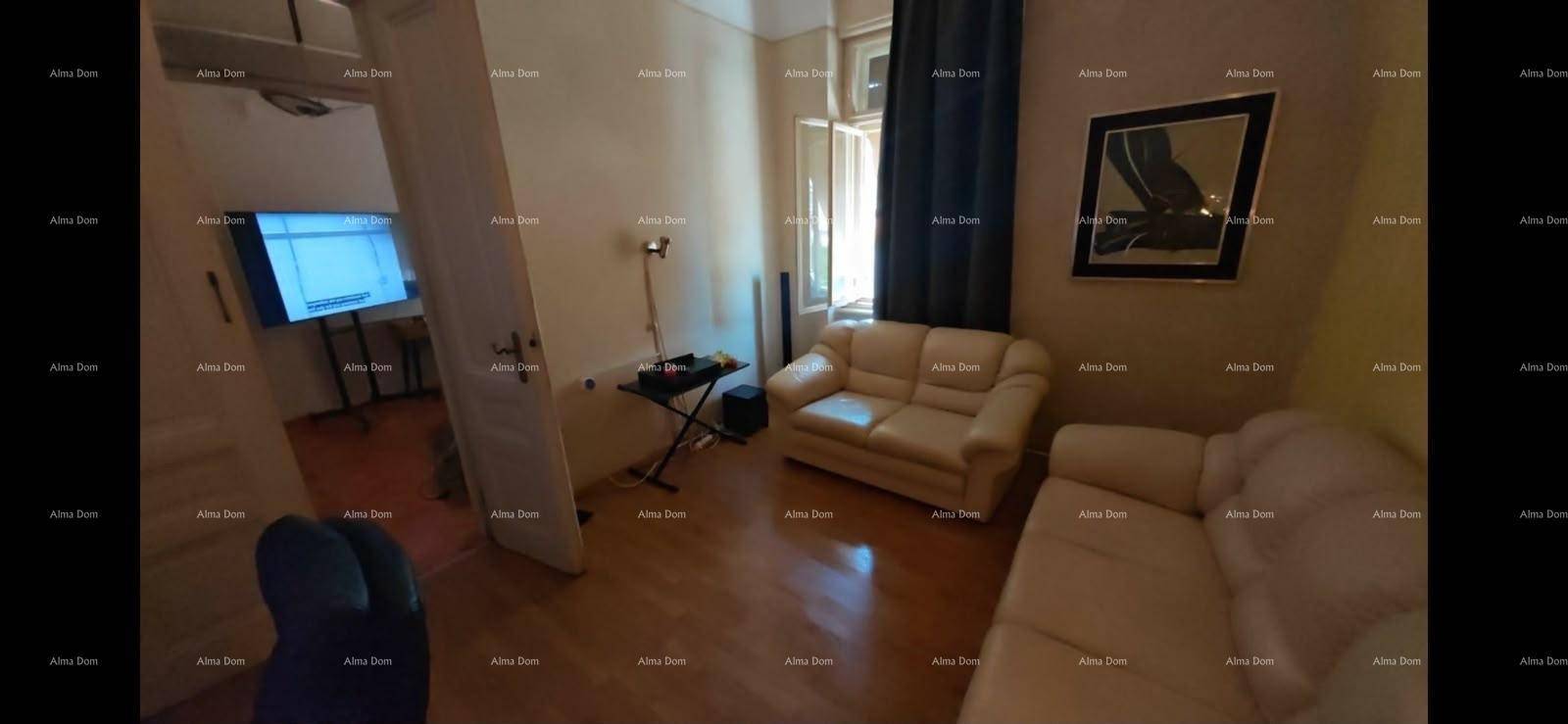 Gemütliches Wohnzimmer mit beigen Sofas und Holzboden, durch eine Tür ist ein Fernseher sichtbar.