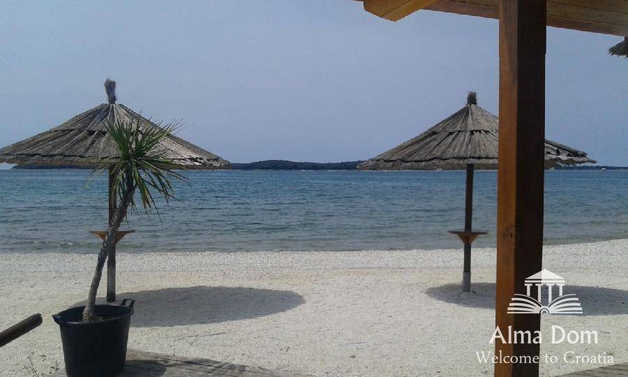 Sandstrand mit zwei Strohschirmen und klarem blauem Meer im Hintergrund, einladend und sonnig.