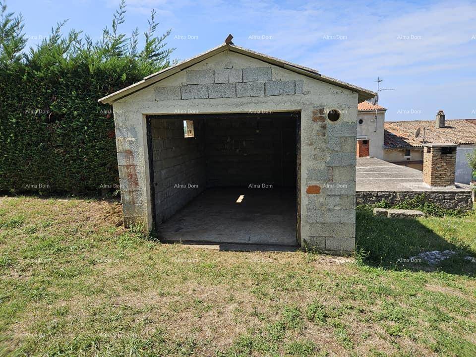 Leere Garage aus Betonblöcken mit Satteldach auf einem grasbewachsenen Grundstück in ländlicher Umgebung.