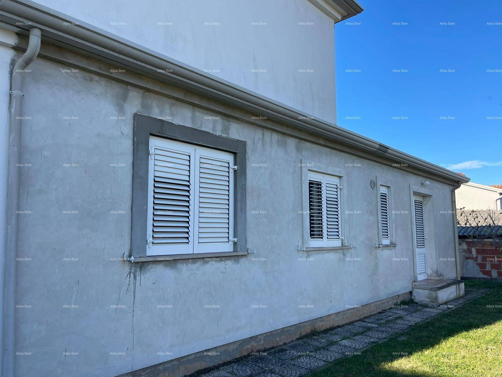 Lange Seitenfassade des Hauses mit mehreren Fenstern, weißen Fensterläden und einer Außentür.