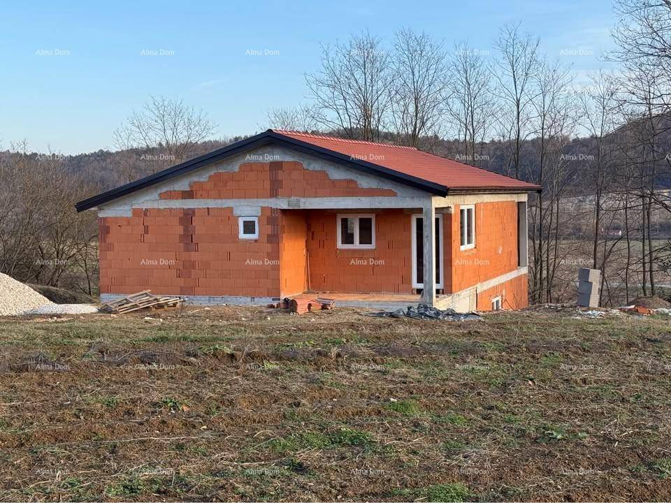 Frontansicht des im Bau befindlichen Hauses mit Ziegelwänden und provisorischem Dach in grüner Umgebung.