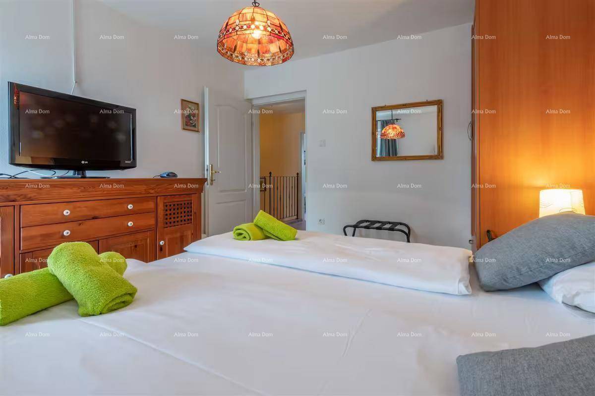 Schlafzimmer mit großem Bett, Holzkommode, Fernseher und dekorativer Deckenleuchte.