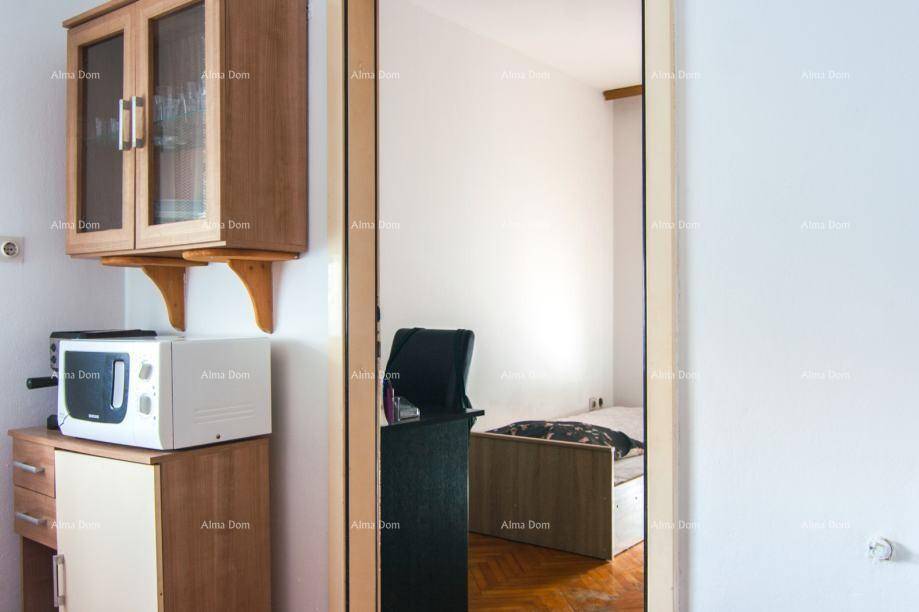 Kleine Küchenzeile mit Mikrowelle und Schränken, daneben ein Blick ins Schlafzimmer.