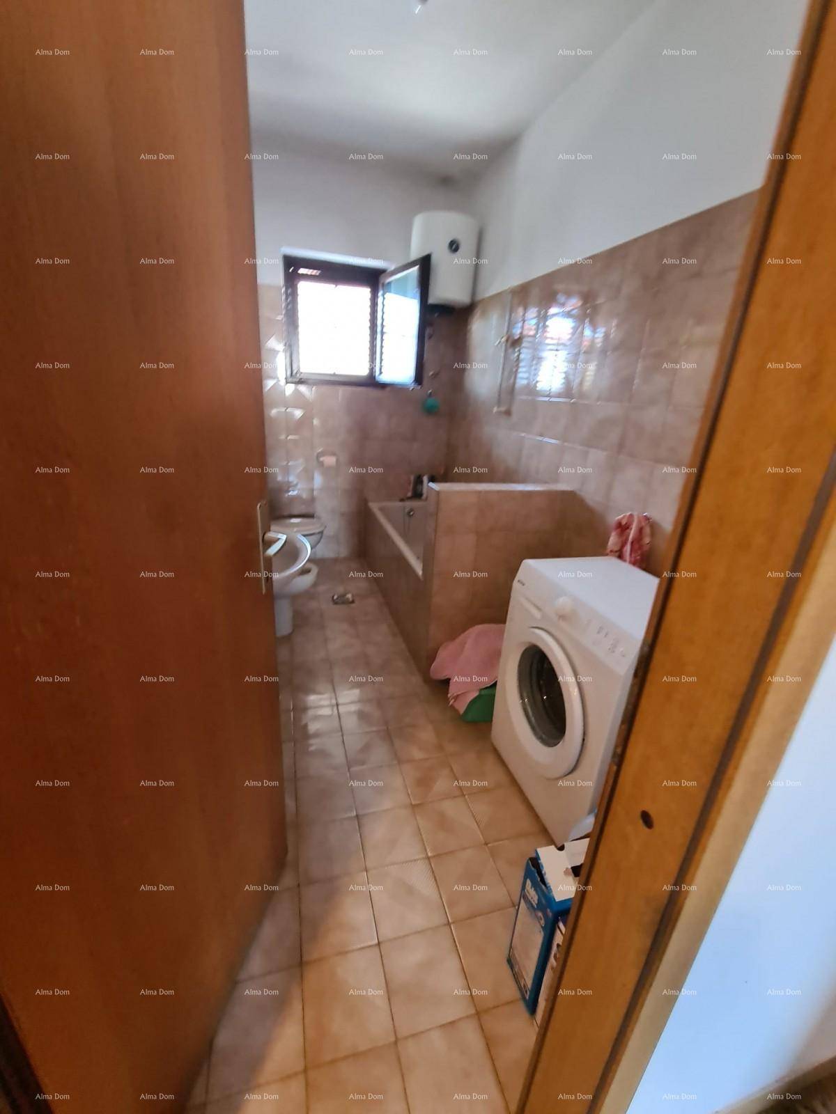 Badezimmer mit beigen Fliesen, Badewanne und Waschmaschine, durch eine offene Tür sichtbar.