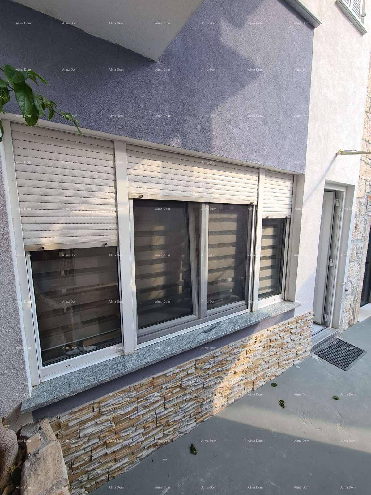 Fassadendetail mit Fenstern, Rollläden und dekorativer Steinverkleidung am Sockel.