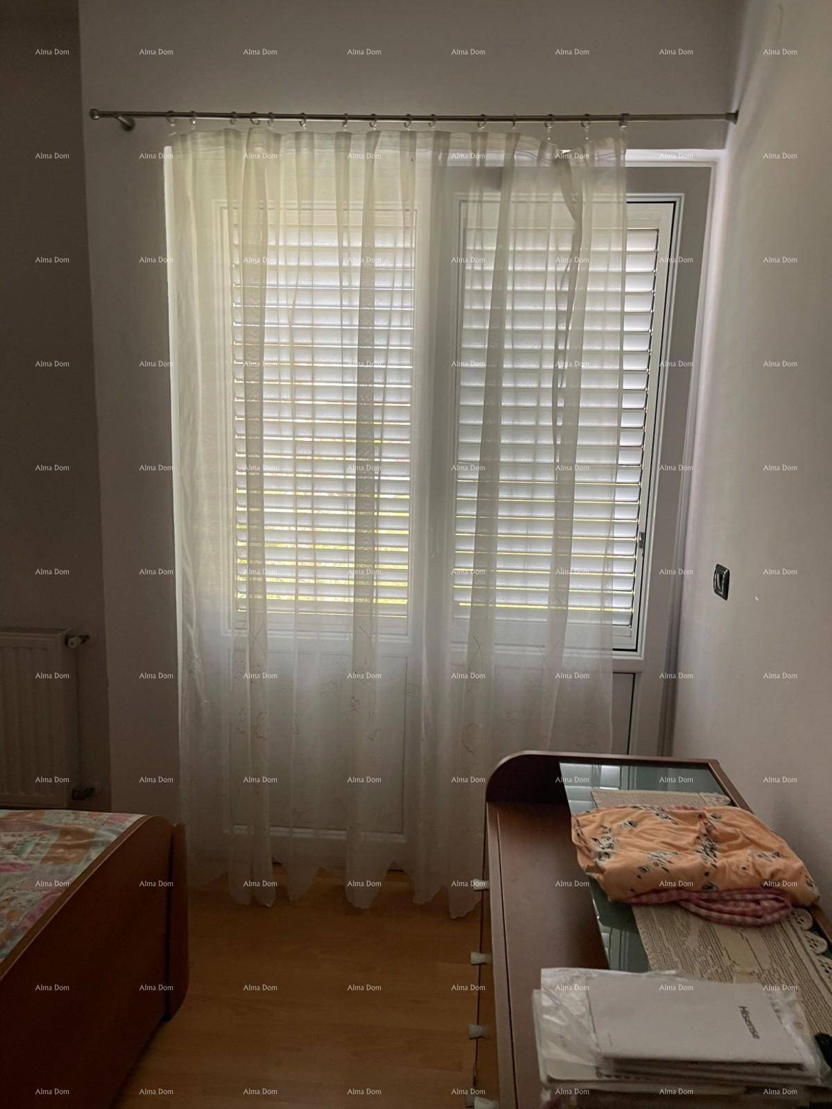 Schlafzimmer mit einem großen Fenster, das von hellen Vorhängen verdeckt wird und Tageslicht hereinlässt.
