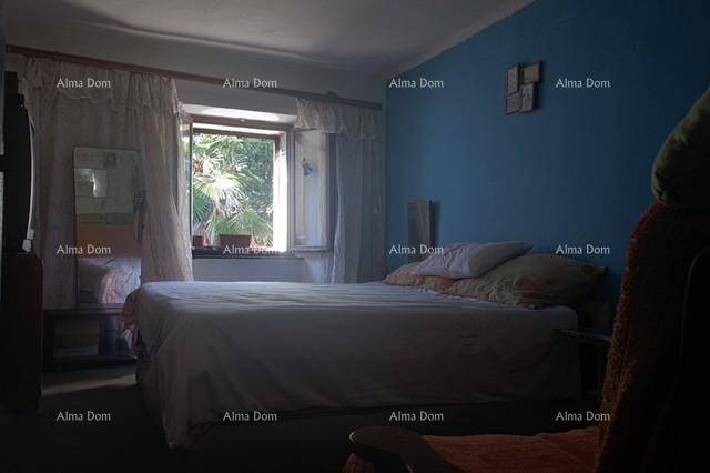 Schlafzimmer mit Doppelbett und blauer Wand, das durch das Fenster einen Blick ins Grüne bietet.