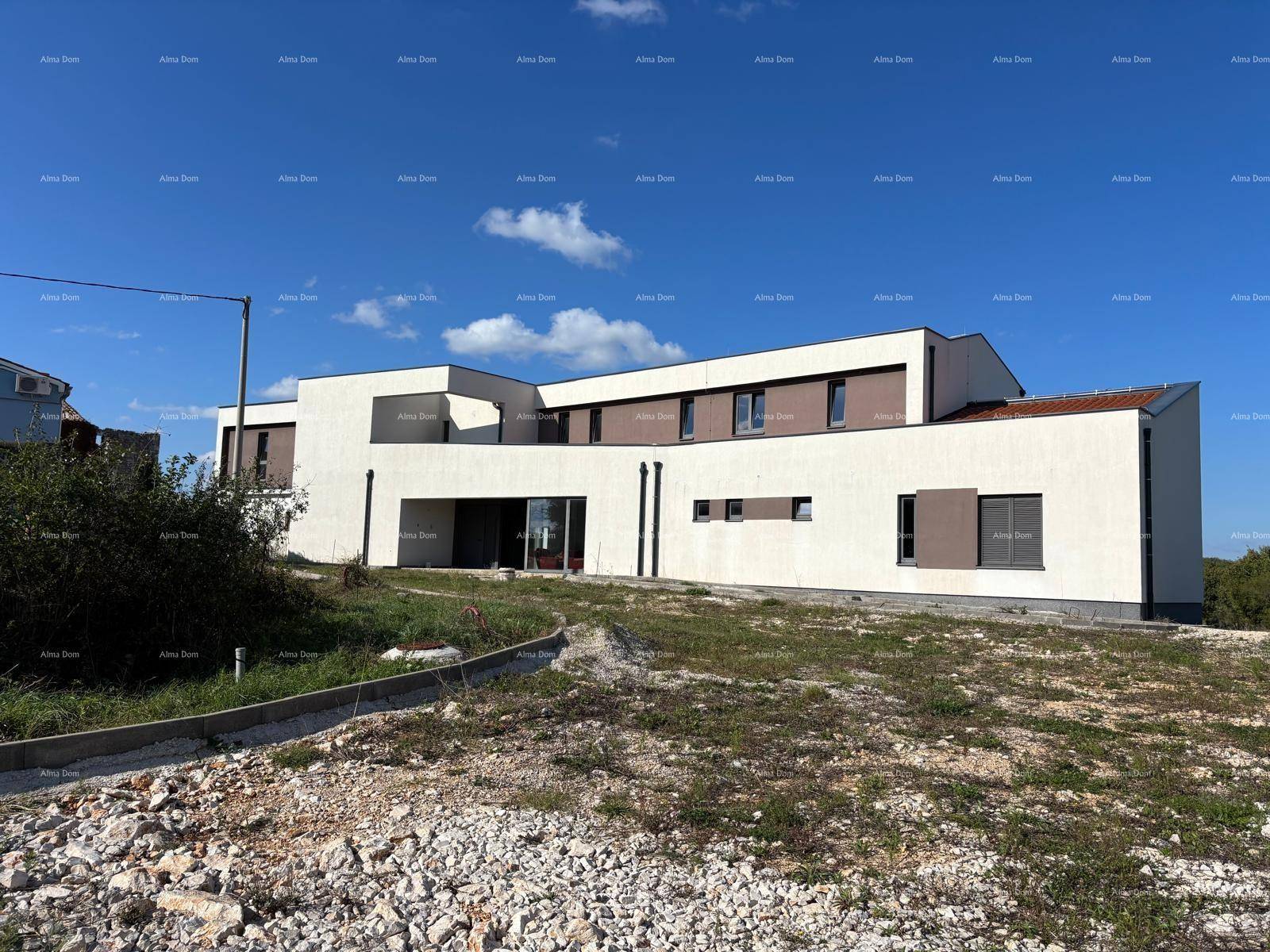 Moderne Hausfassade mit großen Fenstern und braunen Akzenten, umgeben von unfertigem Gelände.