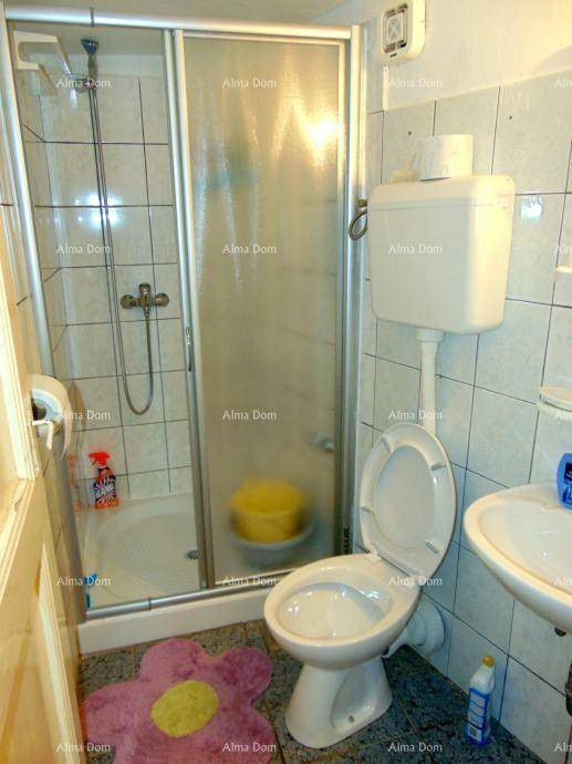 Kleines Badezimmer mit Duschkabine, Toilette und Waschbecken, komplett gefliest.