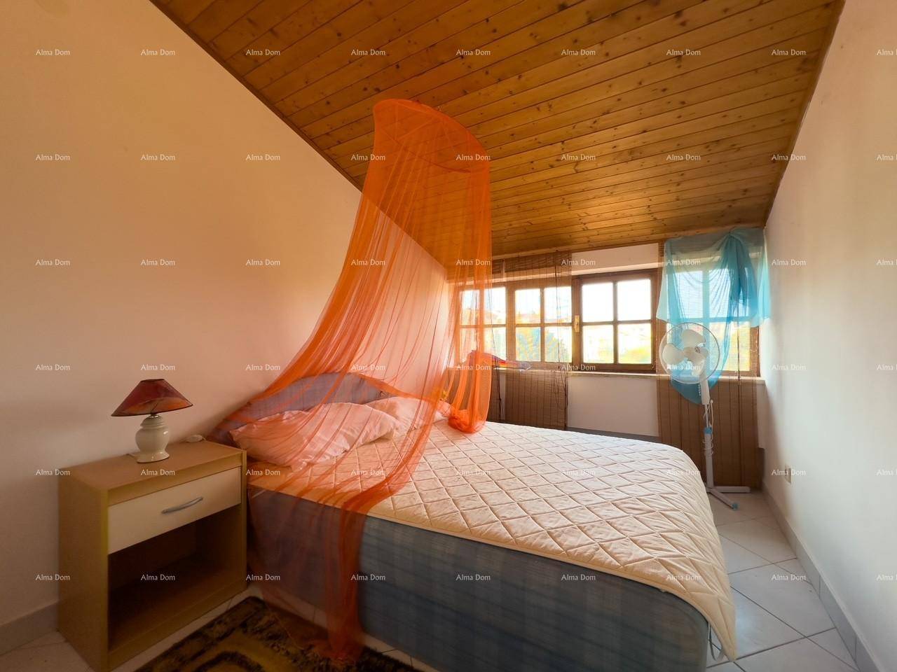 Schlafzimmer mit Holzbalkendecke, Doppelbett und einem orangefarbenen Moskitonetz.