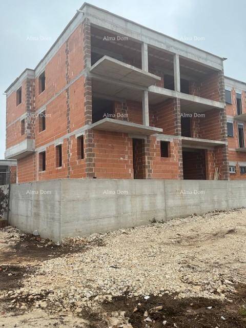 Neubau im Rohbau mit sichtbaren Ziegelwänden und Betonstrukturen auf einem unebenen Grundstück.