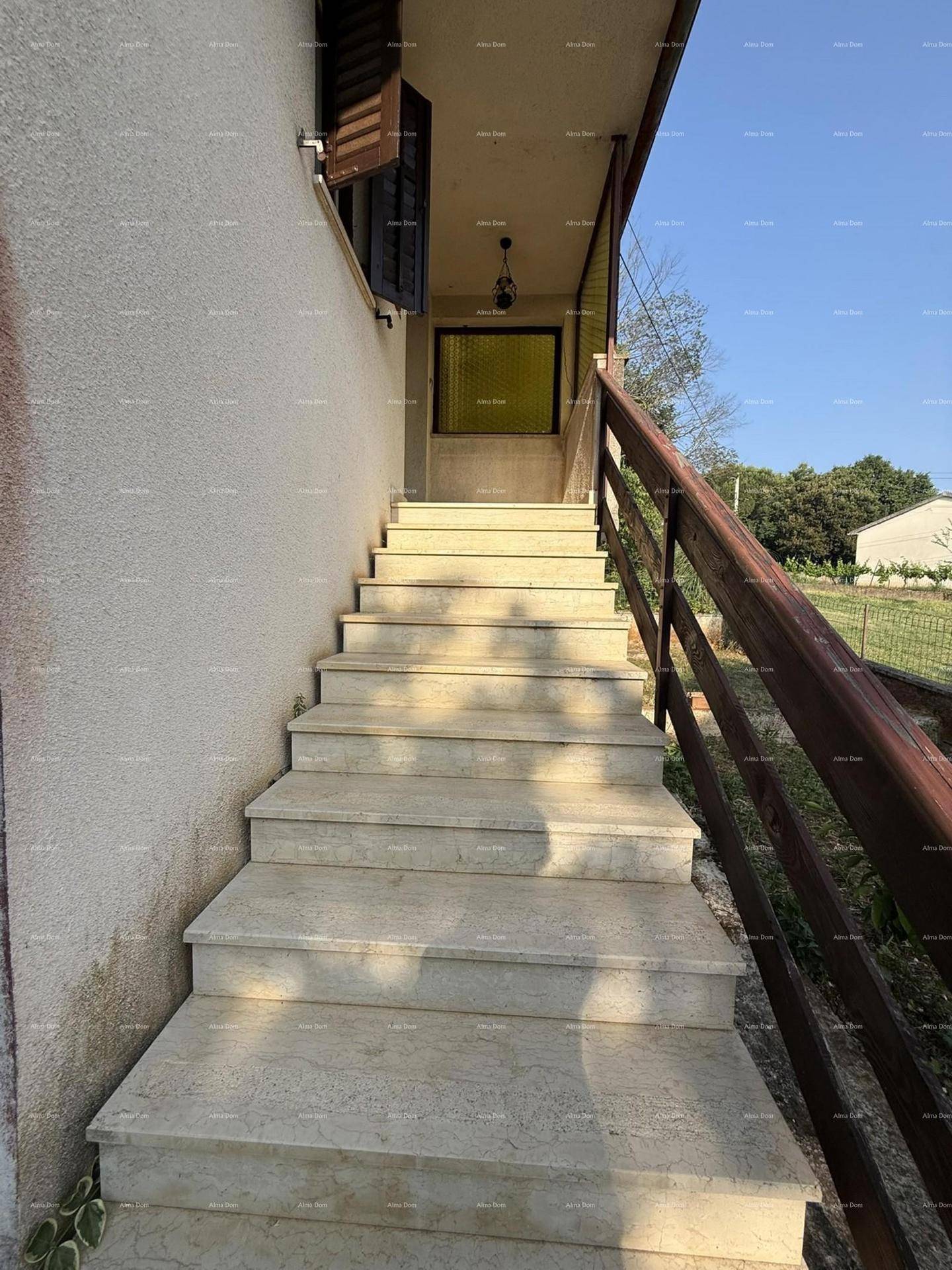 Steintreppe mit Holzgeländer führt zum Eingang des Hauses im Obergeschoss.