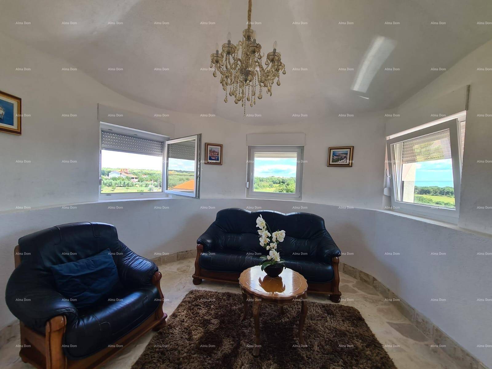Rundes Wohnzimmer mit Ledersofas, Kronleuchter und weitem Blick auf die Landschaft.
