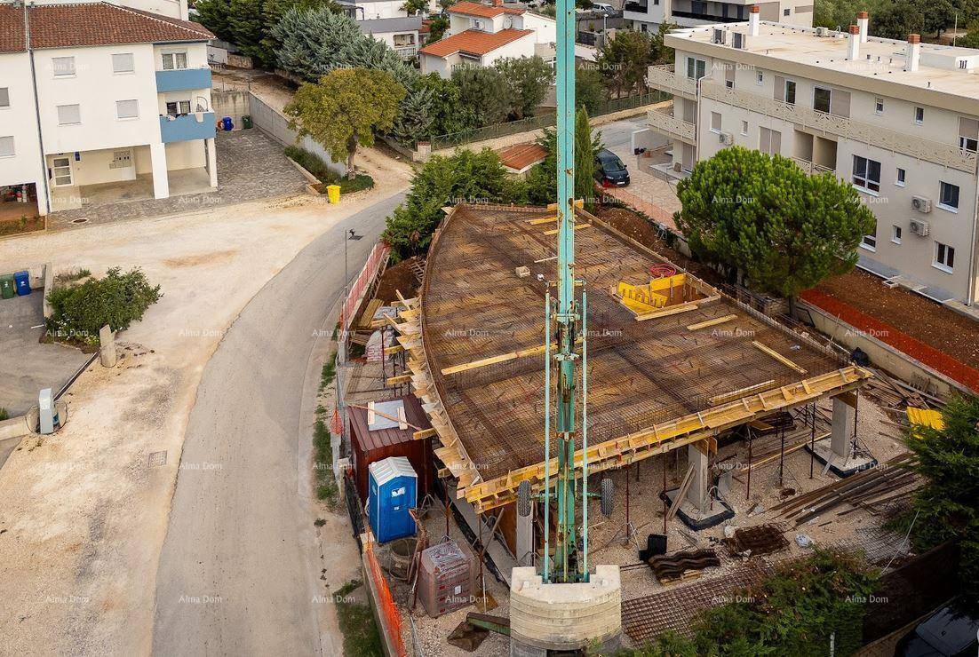 Baustelle mit einem Betonpumpenarm und dem Rohbau, umgeben von weiteren Wohngebäuden und Bäumen.