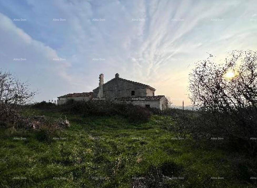 Altes Steinhaus auf einem Hügel bei Sonnenuntergang, umgeben von grüner Landschaft und Büschen.