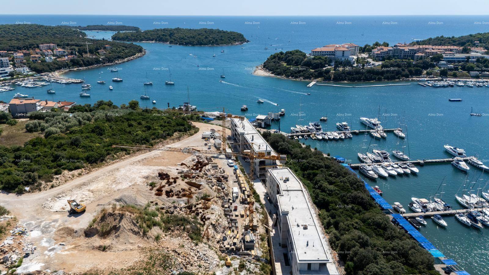 Luftaufnahme einer Baustelle mit im Bau befindlichen Gebäuden und einem Yachthafen mit vielen Booten.