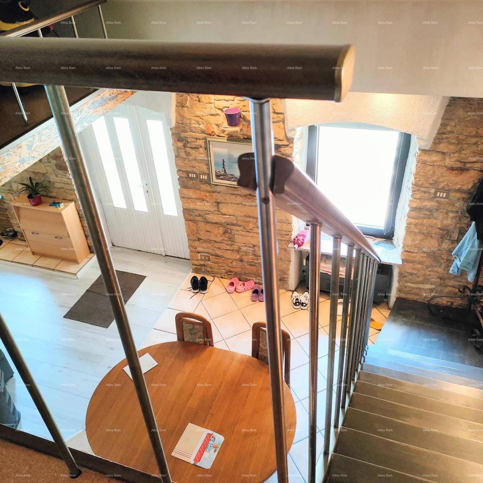 Blick von der Treppe auf den offenen Wohn- und Essbereich mit rundem Holztisch und Steinfliesenboden.