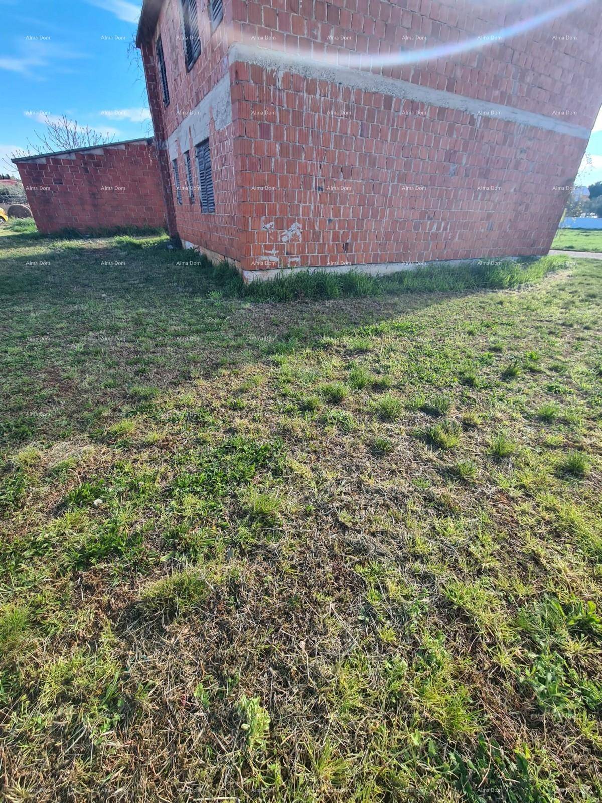 Nahaufnahme des Fundaments des Ziegelgebäudes mit Grasbewuchs im Vordergrund.