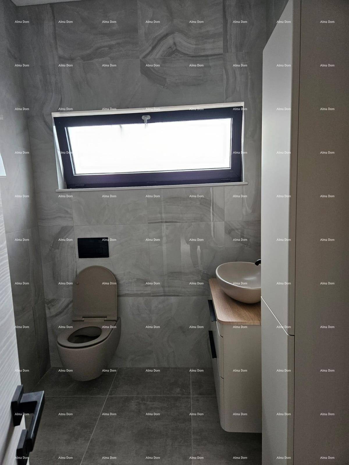 Modernes Badezimmer mit grauen Fliesen, wandhängendem WC, Einzelwaschbecken und Fenster für Tageslicht.