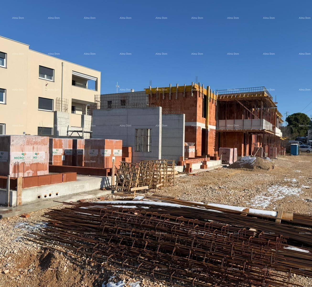 Übersicht der Baustelle mit Rohbauten, Baumaterialien und einem angrenzenden Gebäude.