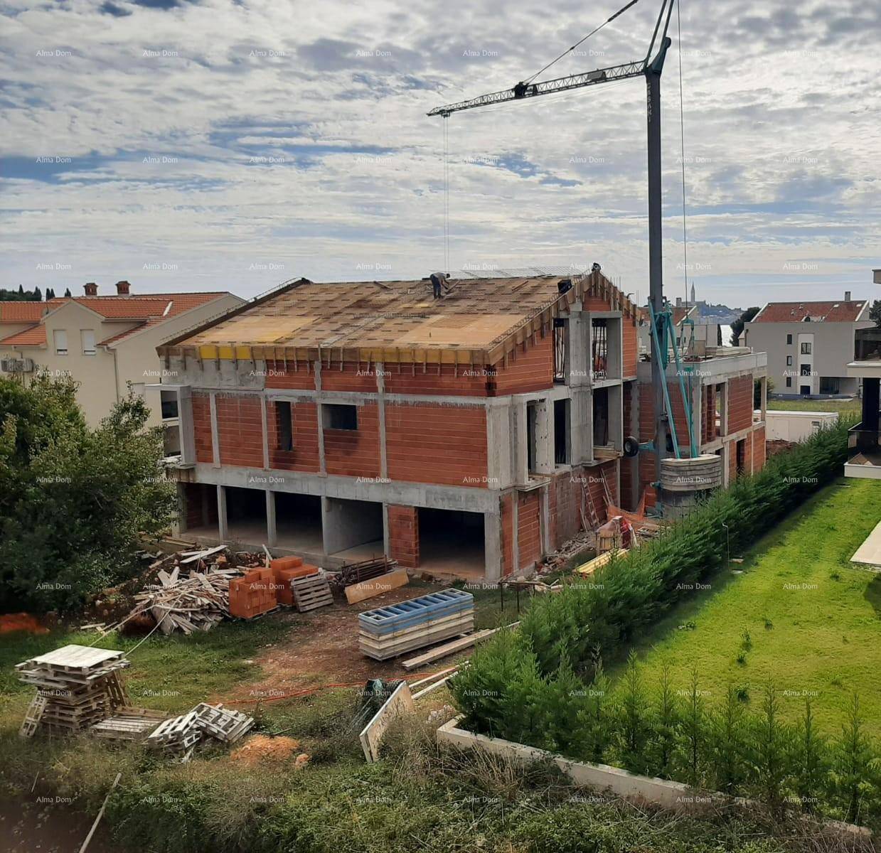 Baustelle eines Hauses mit Rohbau, Ziegelwänden und einem Kran, im Hintergrund das Meer.