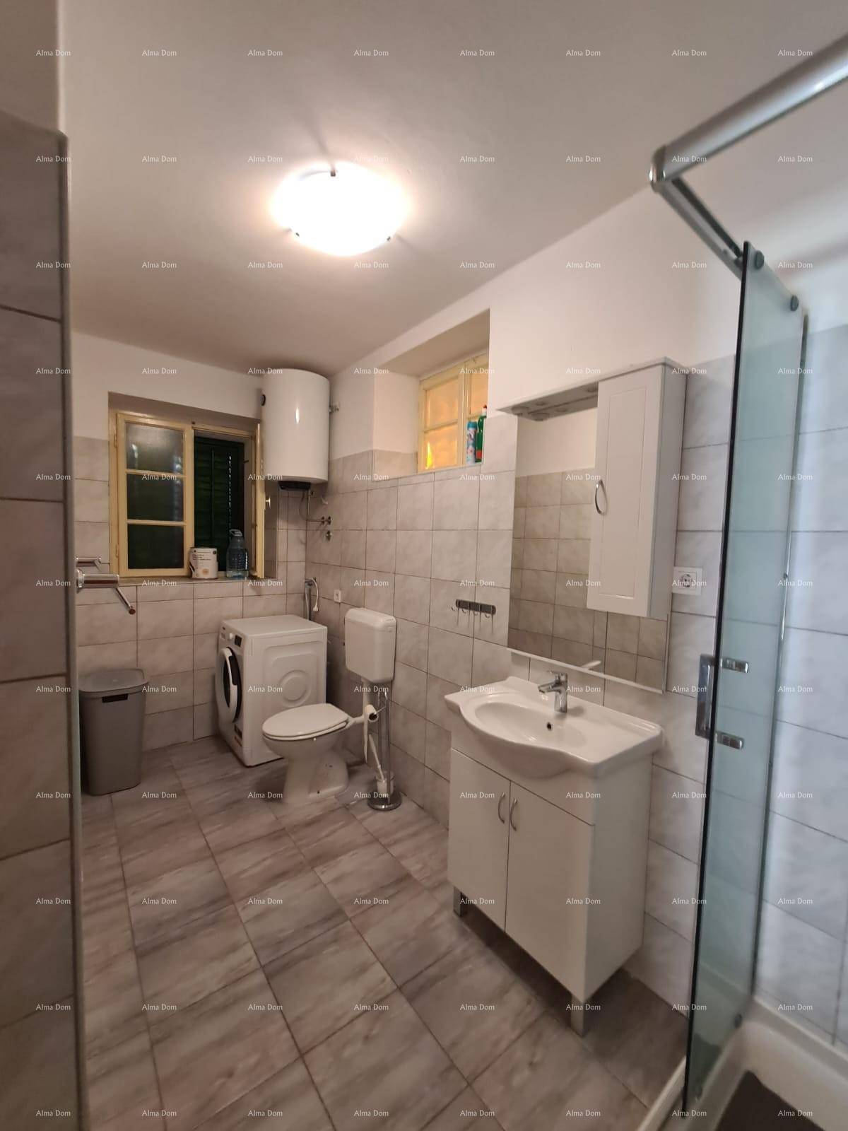 Geräumiges Badezimmer mit Dusche, Waschmaschine, Toilette und Fenster, in hellen Fliesen gehalten.