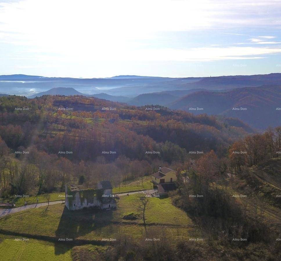 Luftaufnahme eines verfallenen Gebäudes und eines weiteren Hauses in einer hügeligen, bewaldeten Landschaft.