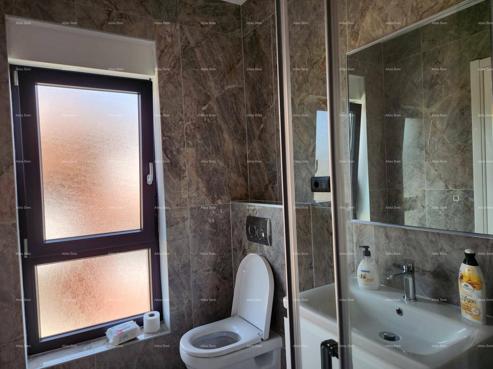 Modernes Badezimmer mit Wand-WC, Waschbecken, Spiegel und Fenster, gefliest in dunklen Tönen.