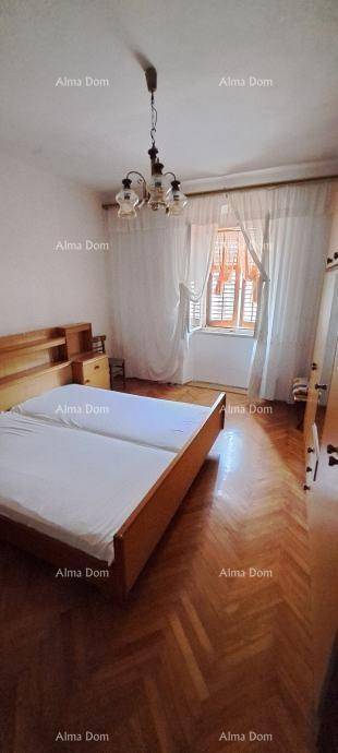 Schlafzimmer mit Doppelbett, Holzparkett und einem Fenster mit Vorhängen.