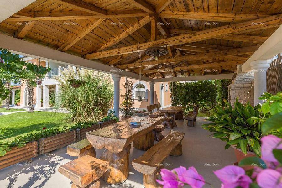 Rustikale überdachte Terrasse mit massivem Holztisch und Bänken, umgeben von üppigem Grün.