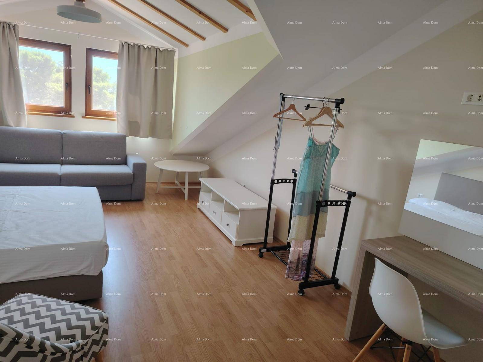 Geräumiges Dachgeschoss-Schlafzimmer mit Holzbalken, Sofa, Bett und praktischem Kleiderständer.