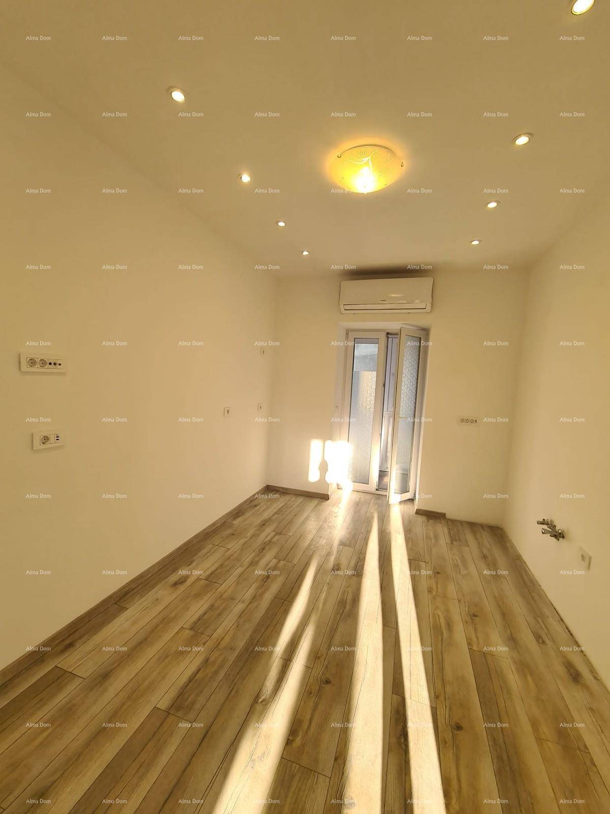 Sonniger Raum mit Holzoptik-Fliesenboden, Klimaanlage und Zugang zu einem Balkon.