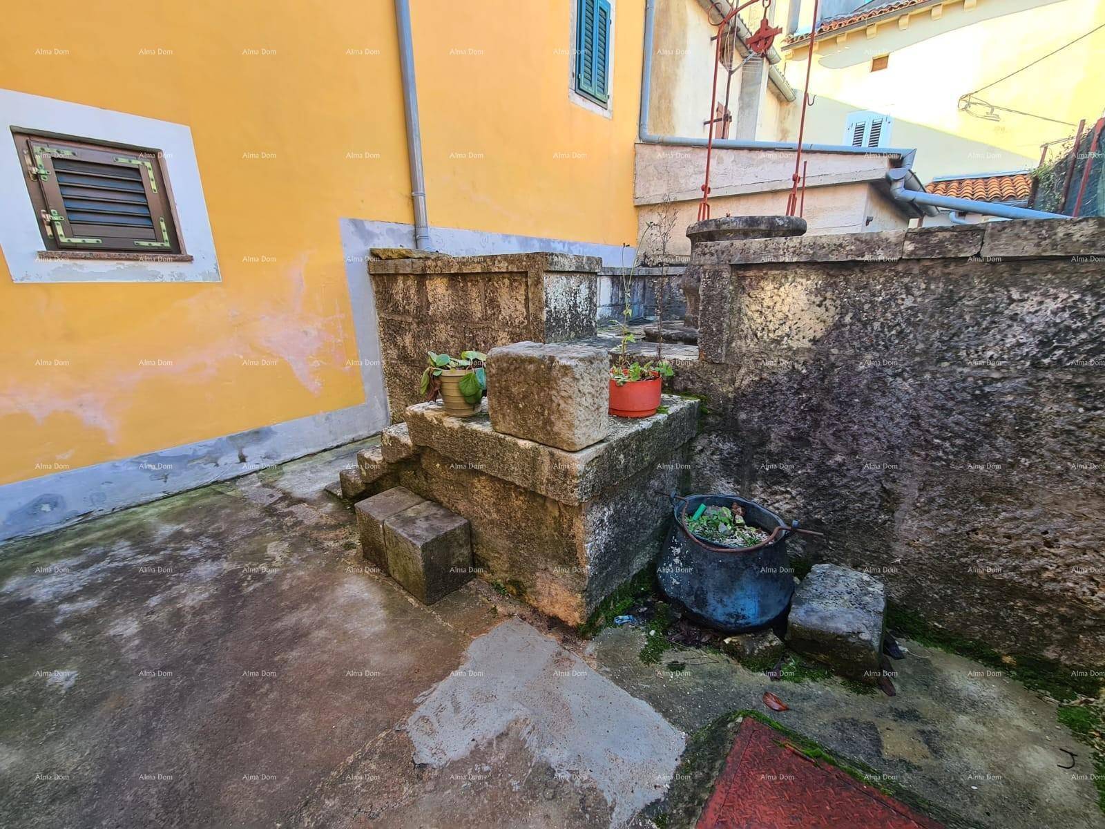 Kleiner, rustikaler Innenhof mit Steinmauern und Pflanzen in Töpfen, umgeben von gelben Fassaden.