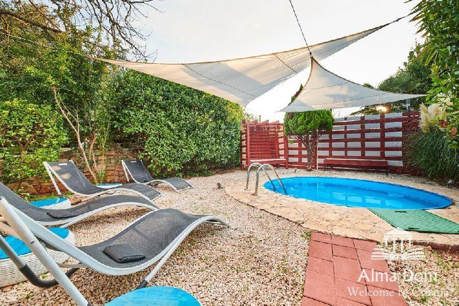 Poolbereich mit Liegestühlen, Sonnensegeln und üppiger grüner Bepflanzung.