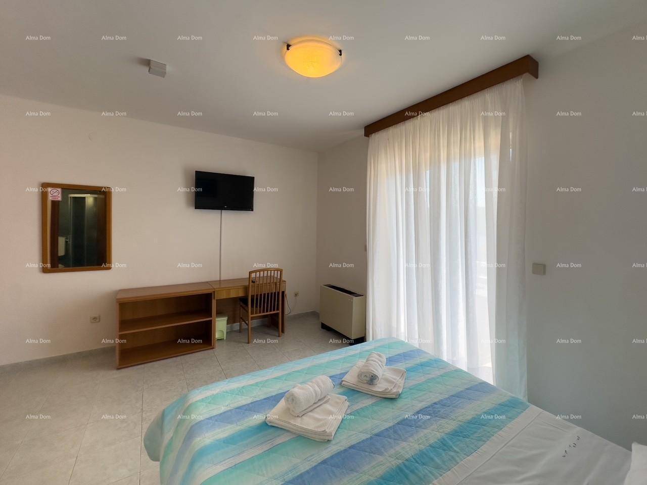 Schlafzimmer mit Doppelbett, Schreibtisch und Flachbildfernseher, hell durch große Fenster mit Vorhängen.